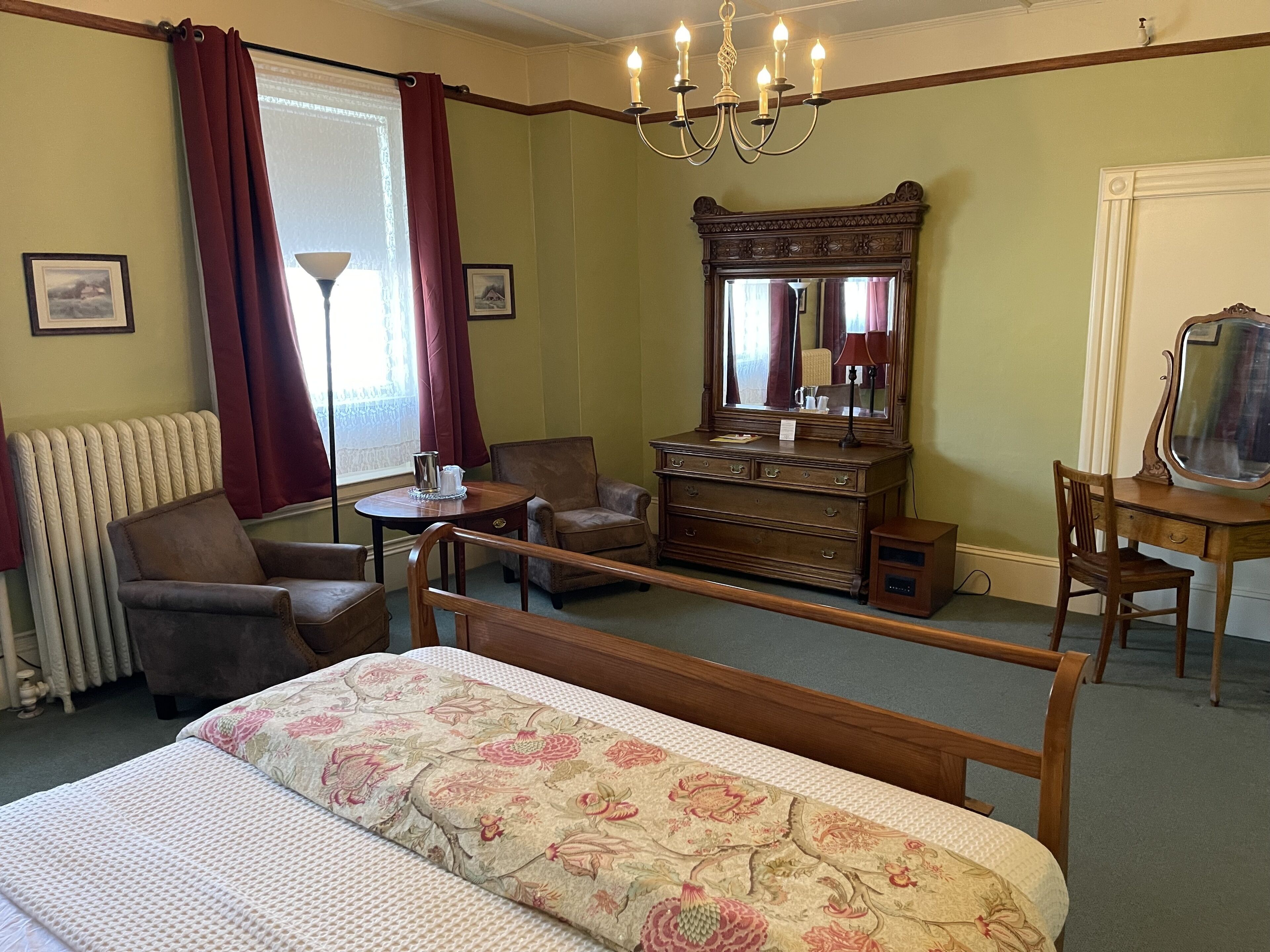 Une pièce comprenant un lit, une commode en bois, une chaise, une petite table et un miroir.