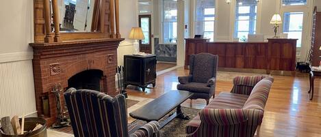 A spacious lobby with a fireplace, striped armchairs, a sofa, a reception desk, and a chandelier.