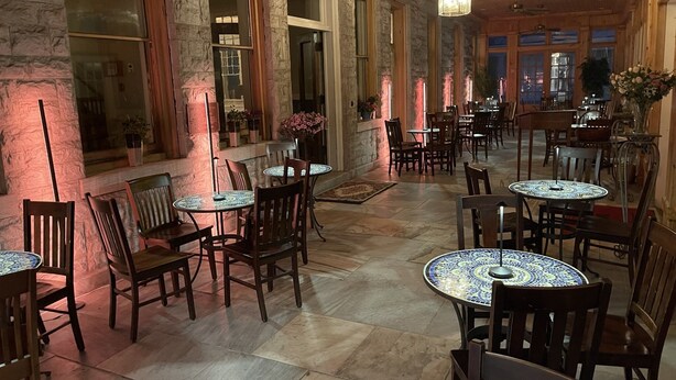 A spacious indoor area with multiple round tables and chairs, stone walls, and large windows.
