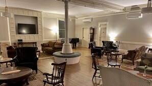 A spacious living room with a large TV, multiple seating options, and a decorative column. - The Brandon Inn - Single Room (Brandon)