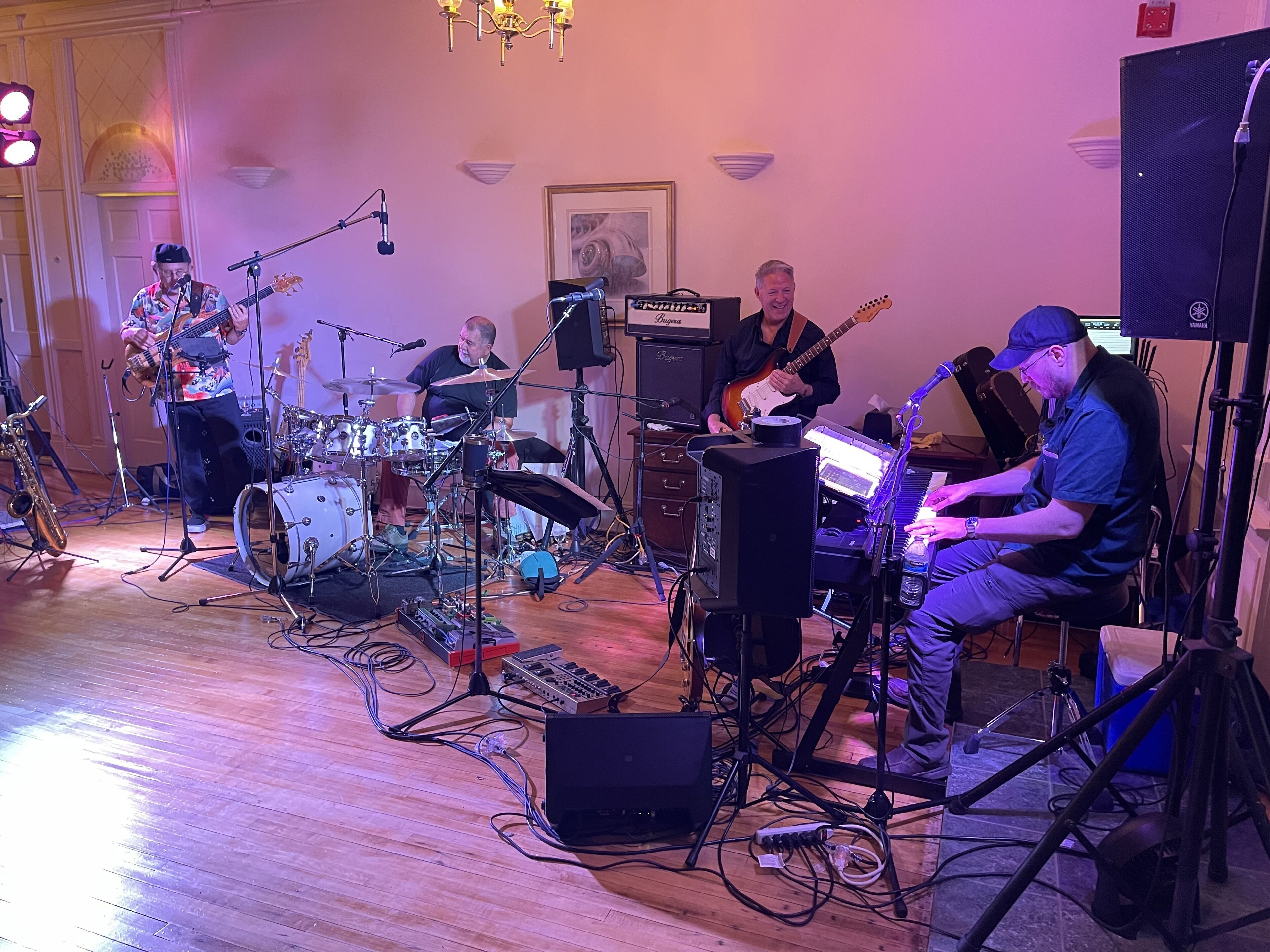 A band performing in a room with a drum set, a keyboard, and a guitar.