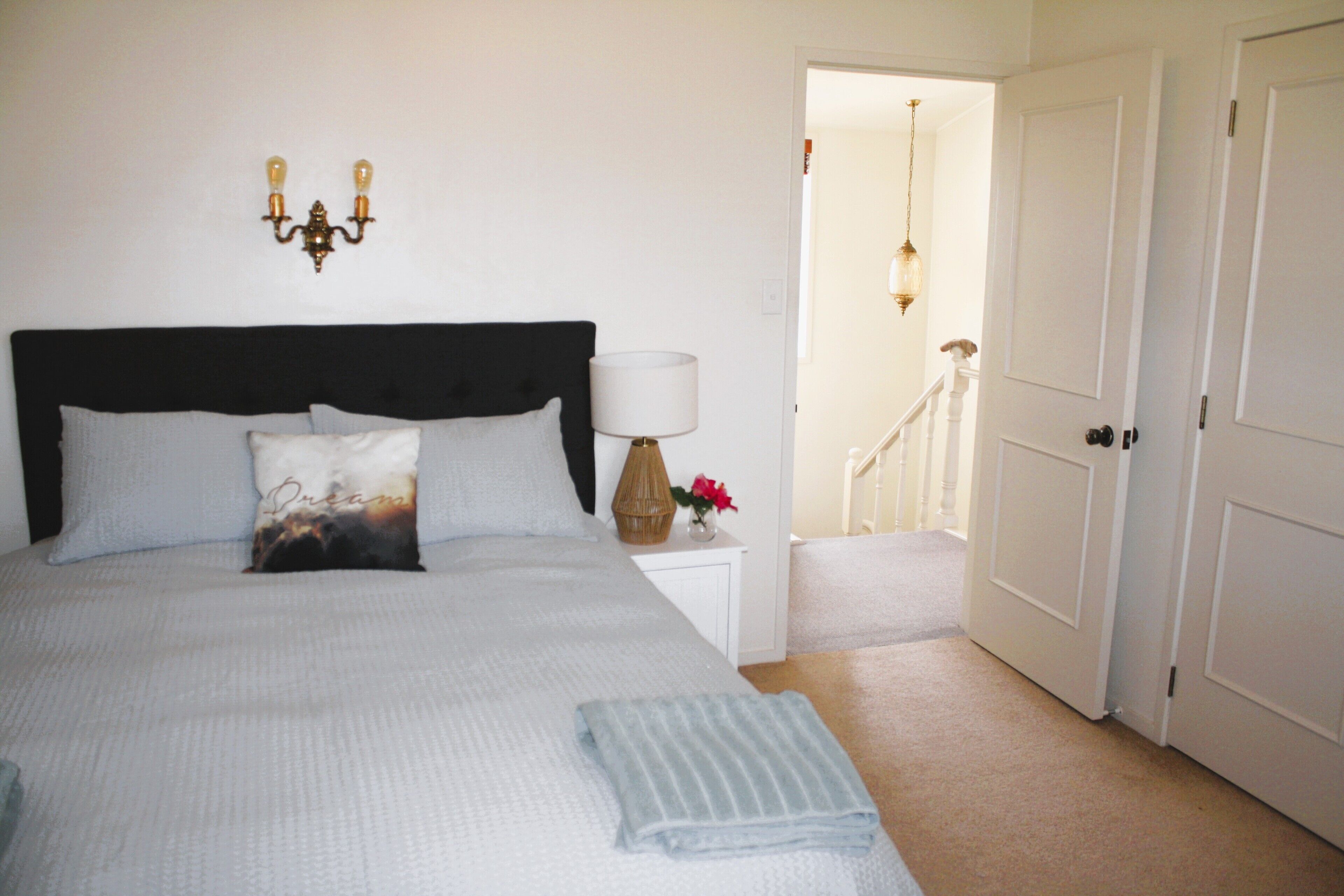 A neatly made bed with a headboard, a bedside lamp, and a small table with a vase of flowers.