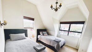 A bedroom with two beds, a chandelier, and a window with a view of the outside. - Mission Bay Beach House. Pet-Friendly (Auckland)