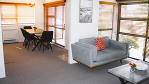 A modern living room with a grey sofa, a coffee table, and a dining area with a table and chairs. - Mission Bay Beach House. Pet-Friendly (Auckland)
