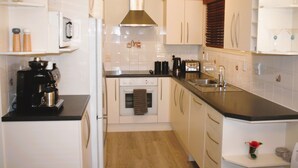 A compact kitchen with white cabinets, a stainless steel range hood, a built-in oven, and a black countertop. - Mission Bay Beach House. Pet-Friendly (Auckland)