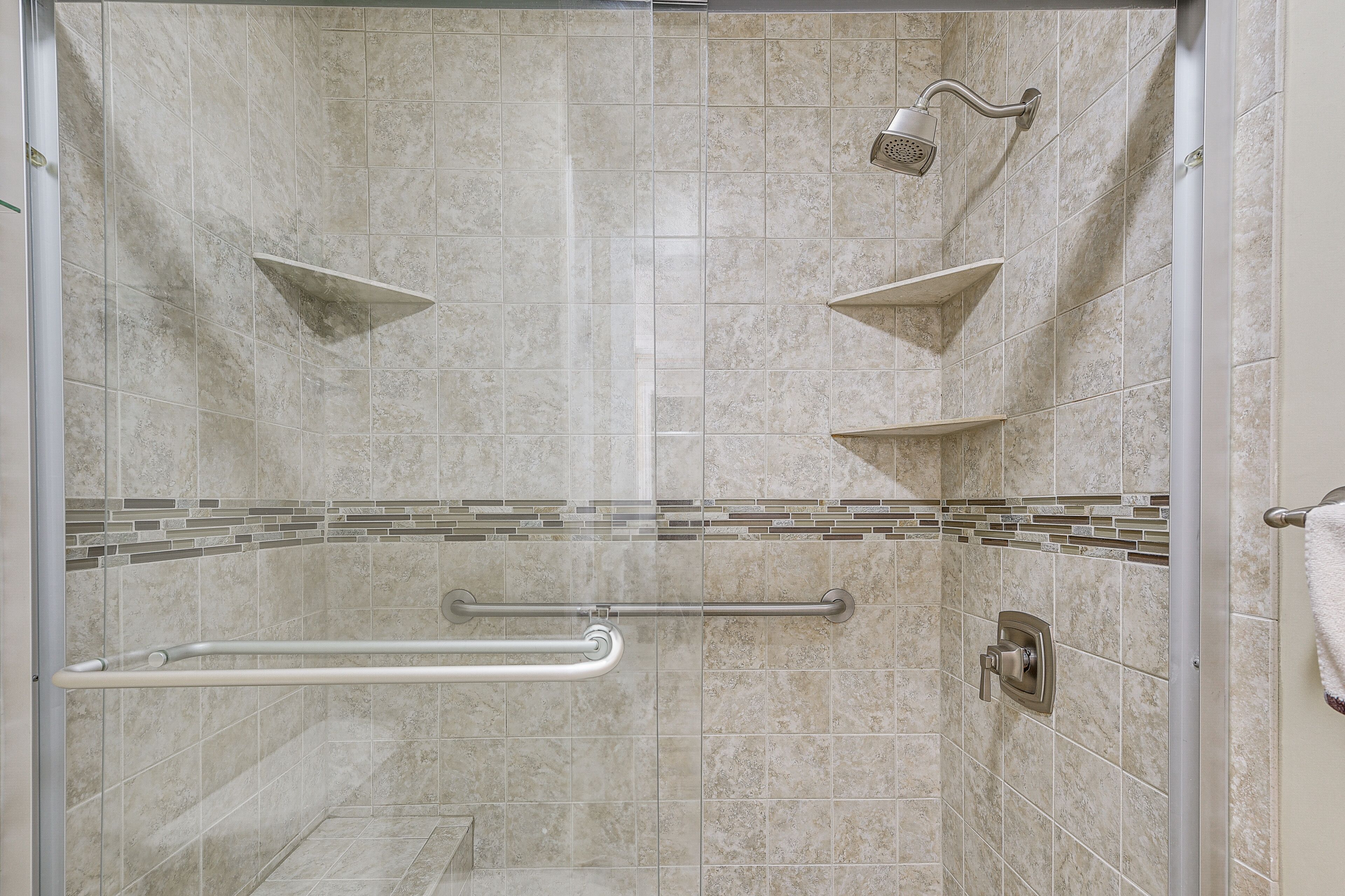 A shower with a handheld showerhead, a grab bar, and a tiled wall.