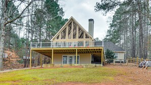 Une maison à deux étages avec un balcon, entourée d’arbres.