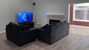 Un salon moderne avec un téléviseur à écran plat, des canapés noirs, une table basse et une cheminée.