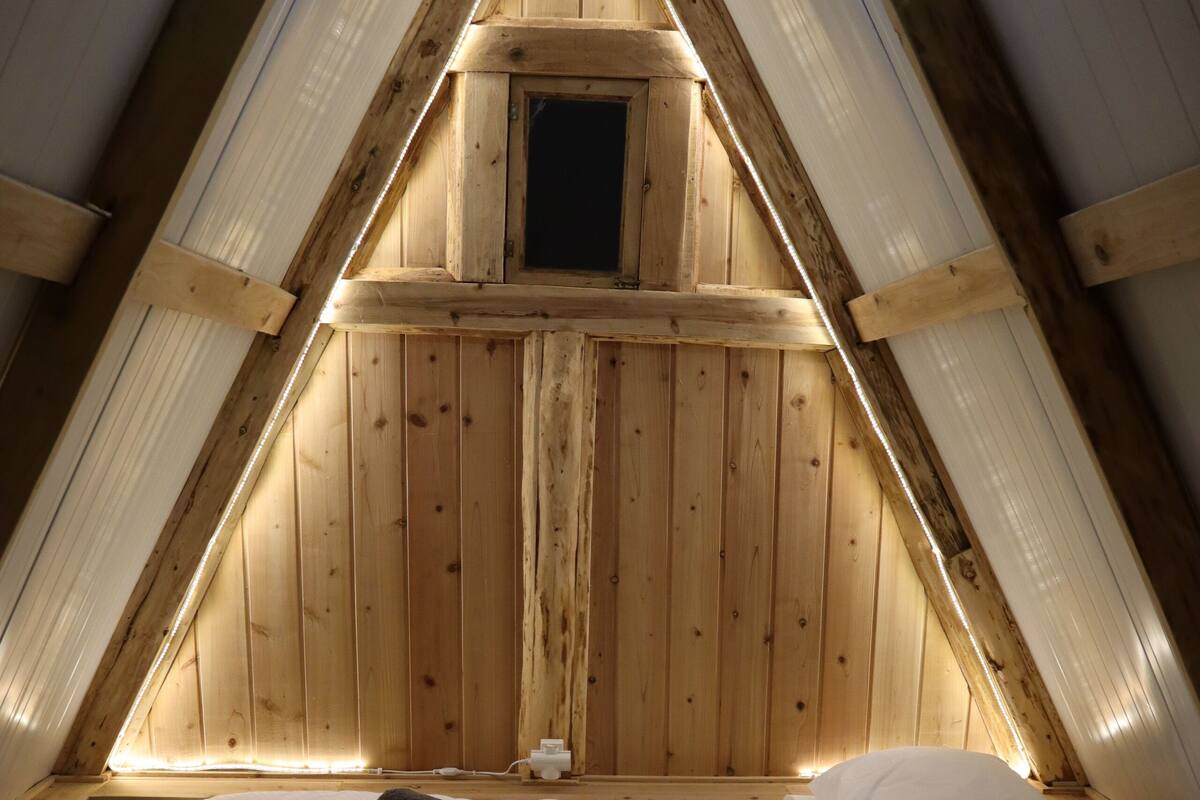 Une pièce triangulaire en bois, avec un lit, deux serviettes enroulées et une petite fenêtre.