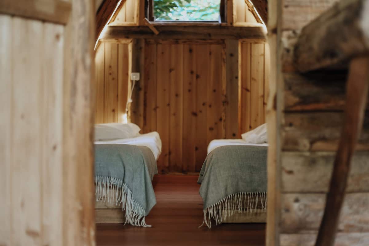 Une pièce de cabane en bois avec deux lits, une fenêtre et un plancher en bois.