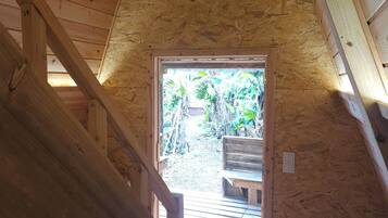 A wooden interior with a sloped ceiling and a view of a garden through a doorway.