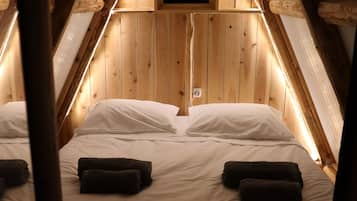 A cozy attic bedroom with a wooden sloped ceiling, a small window, and a neatly made bed with pillows and towels.