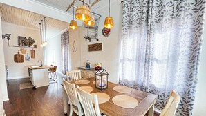 Un espace repas avec une table en bois, des chaises blanches et des lampes suspendues.