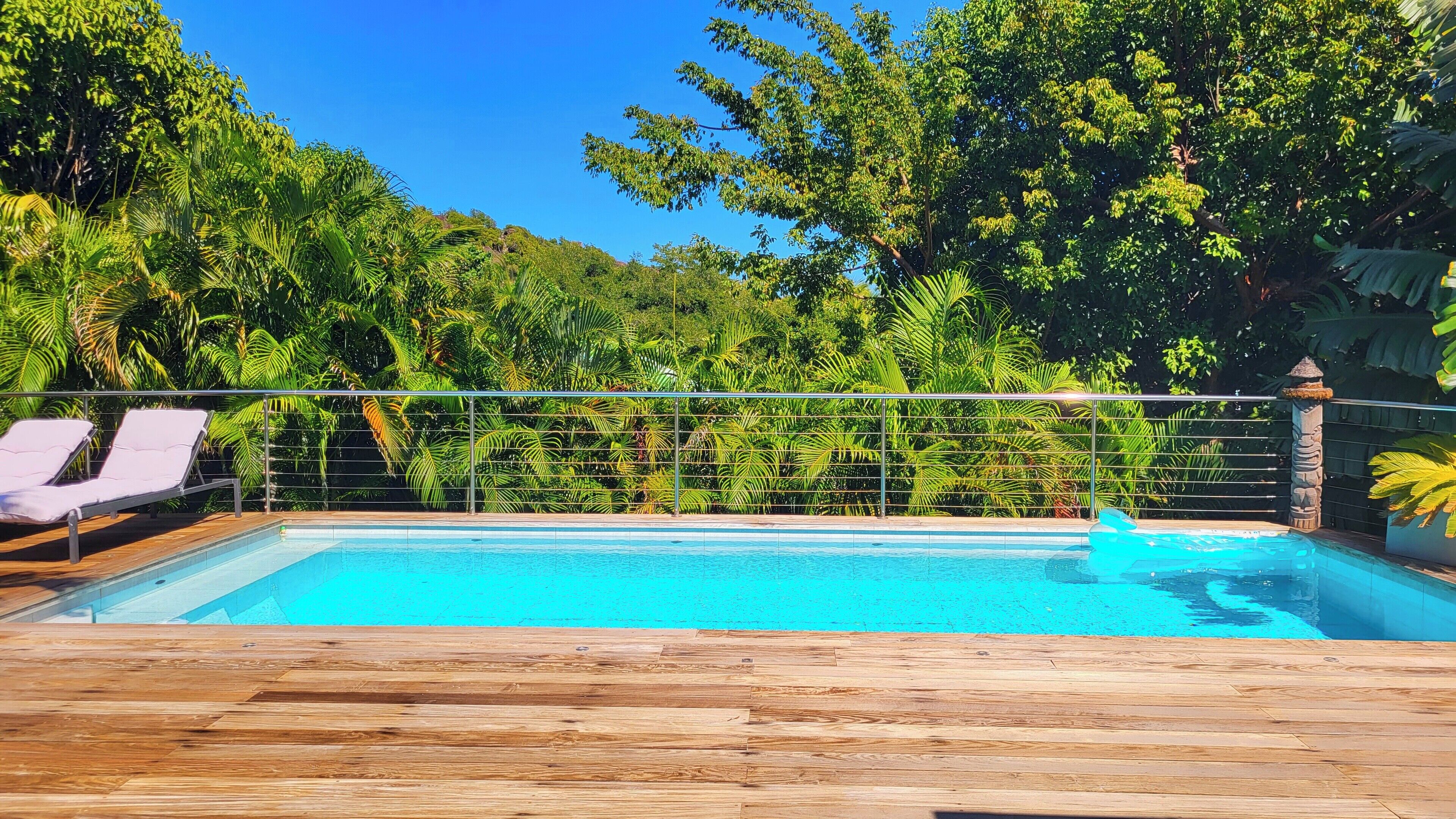 Eine Holzterrasse mit Swimmingpool, umgeben von üppiger Bepflanzung und einem Metallgeländer.