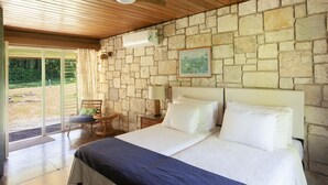 A bedroom with a stone wall, a bed with white linens, a wooden ceiling, and a view through a glass door. - Luxury Three Bedroom Sea View Villa, Frenchman's Cove Resort (Drapers)