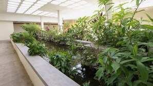 A tranquil indoor garden with a water feature, surrounded by various plants and a skylight above. - Condo Serenity (Portmore)
