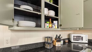 A kitchen with a black granite countertop, a white microwave, a knife block, and a spice rack. - Comfort Cottage (Northport)