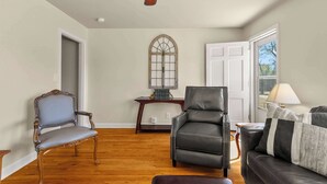 A spacious living room with hardwood flooring, a ceiling fan, a large window, and a fireplace. - Comfort Cottage (Northport)