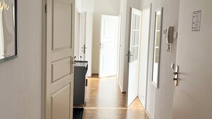 A hallway with white doors, a black bench, and a wooden floor. - Stillvolles 3R Apartment mit Balkon (Leipzig)