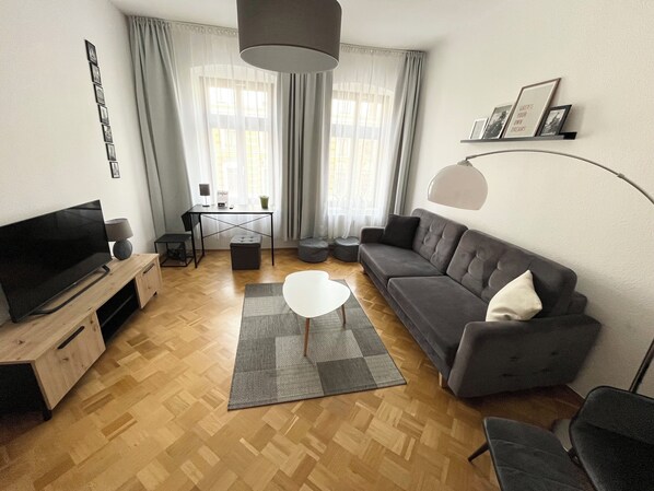Un salon moderne avec un téléviseur à écran plat, un canapé gris, une table basse blanche et un plancher en bois.