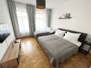 Une chambre d’hôtel avec deux lits, une télévision, un bureau en bois et une étagère murale décorée de tableaux.