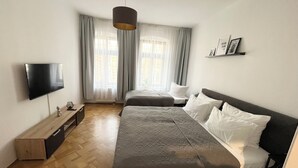A bedroom with a bed, a TV, a bedside table, and a window with curtains. - Stillvolles 3R Apartment mit Balkon (Leipzig)