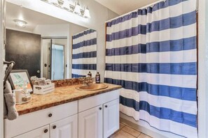 Ein Badezimmer mit gestreiftem Duschvorhang, einem Waschbecken mit Marmorplatte und einem Spiegel darüber.