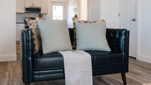 Ein schwarzes Ledersofa mit zwei Kissen, einer weißen Decke und einem gemusterten Kissen.