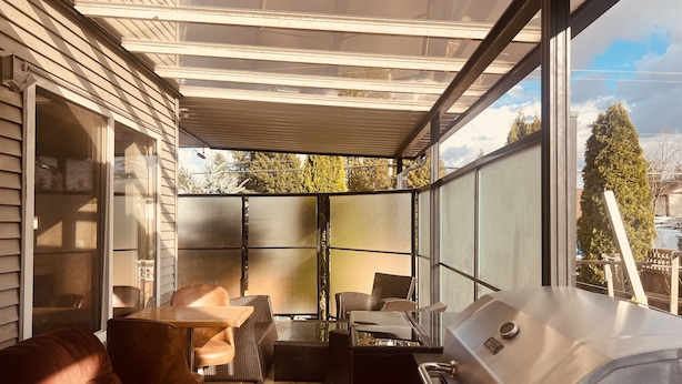 A covered patio with a grill, seating area, and large windows offering views of the surrounding area. - RVH'S Rm #2 /Private Bathroom 
Main Floor area Shared Living Space  (Surrey)
