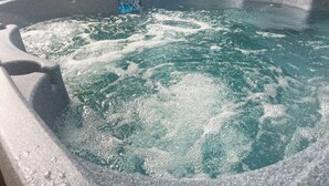 A hot tub with water, a control panel, and a wooden fence in the background.