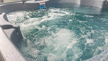 A hot tub with water, a control panel, and a wooden fence in the background.
