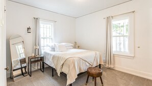 A bedroom with a bed, a bedside table, a mirror, a window, and a door.
