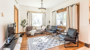 A modern living room with a flat-screen TV, leather sofas, a patterned rug, and large windows with curtains.