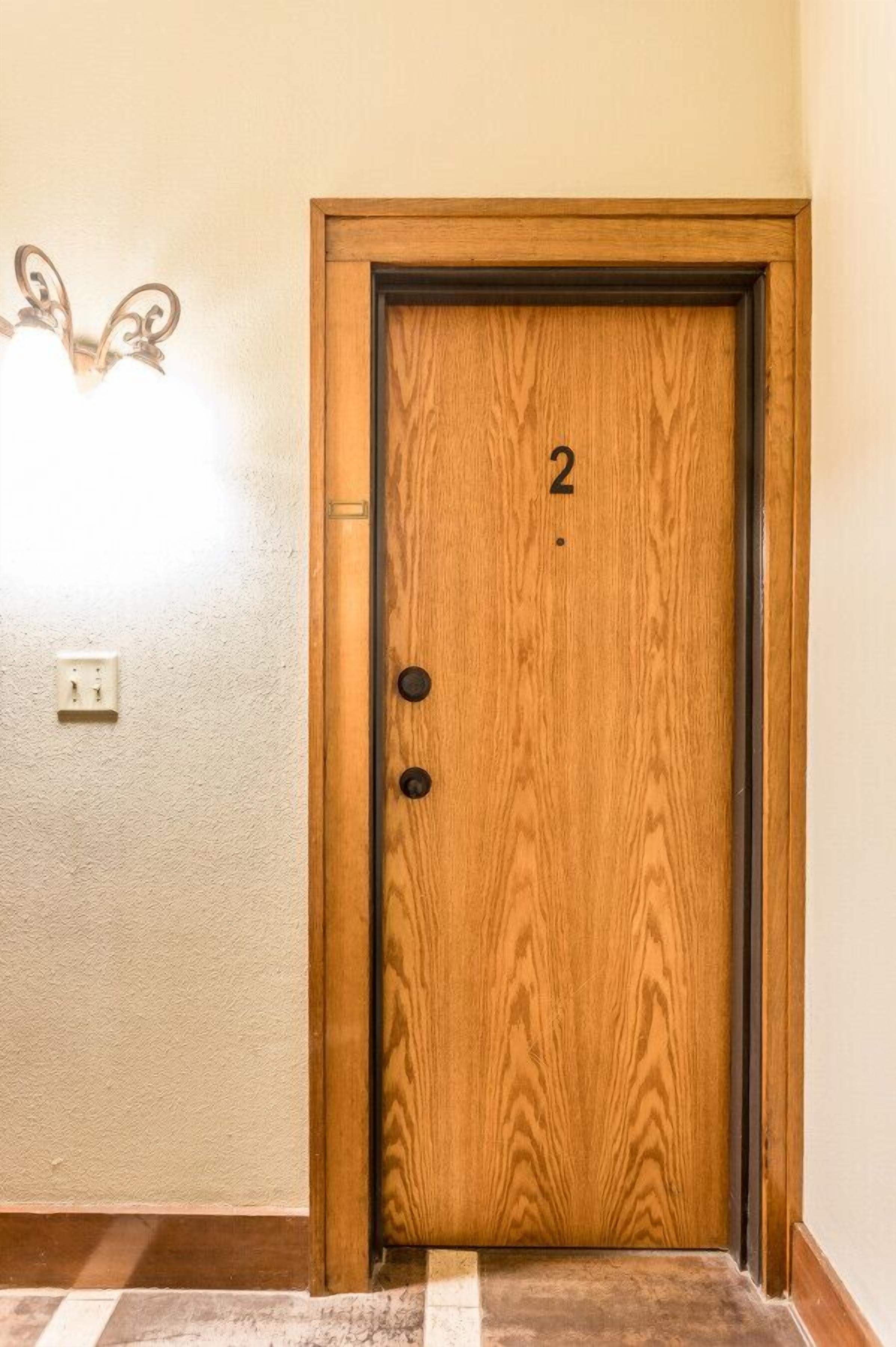 Une porte en bois portant le numéro 2, un interrupteur et un luminaire fixé au mur.