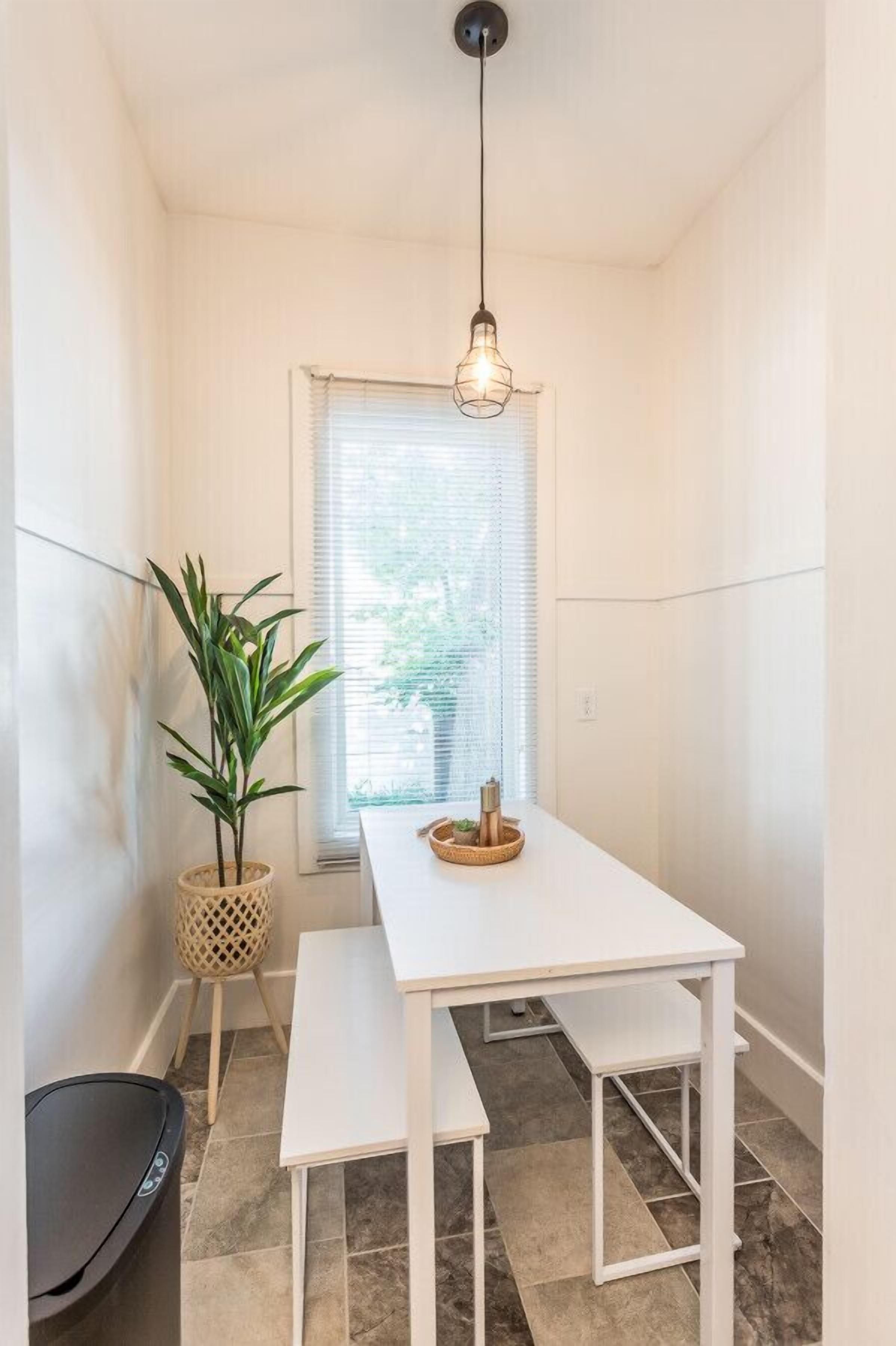 A narrow room with a white table, bench, and hanging light fixture.