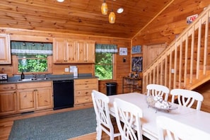 A wooden cabin interior with a kitchen, dining area, and staircase. - Charley's Cabin - Mountain Vacation. Beautiful log cabin on almost 3 acres. (Waynesville)