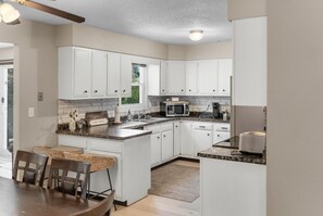 A kitchen with white cabinets, a microwave, a toaster, and a dining area with a table and chairs. - Heartland Haven: A 4-Bed Delight in Sioux Falls (Sioux Falls)