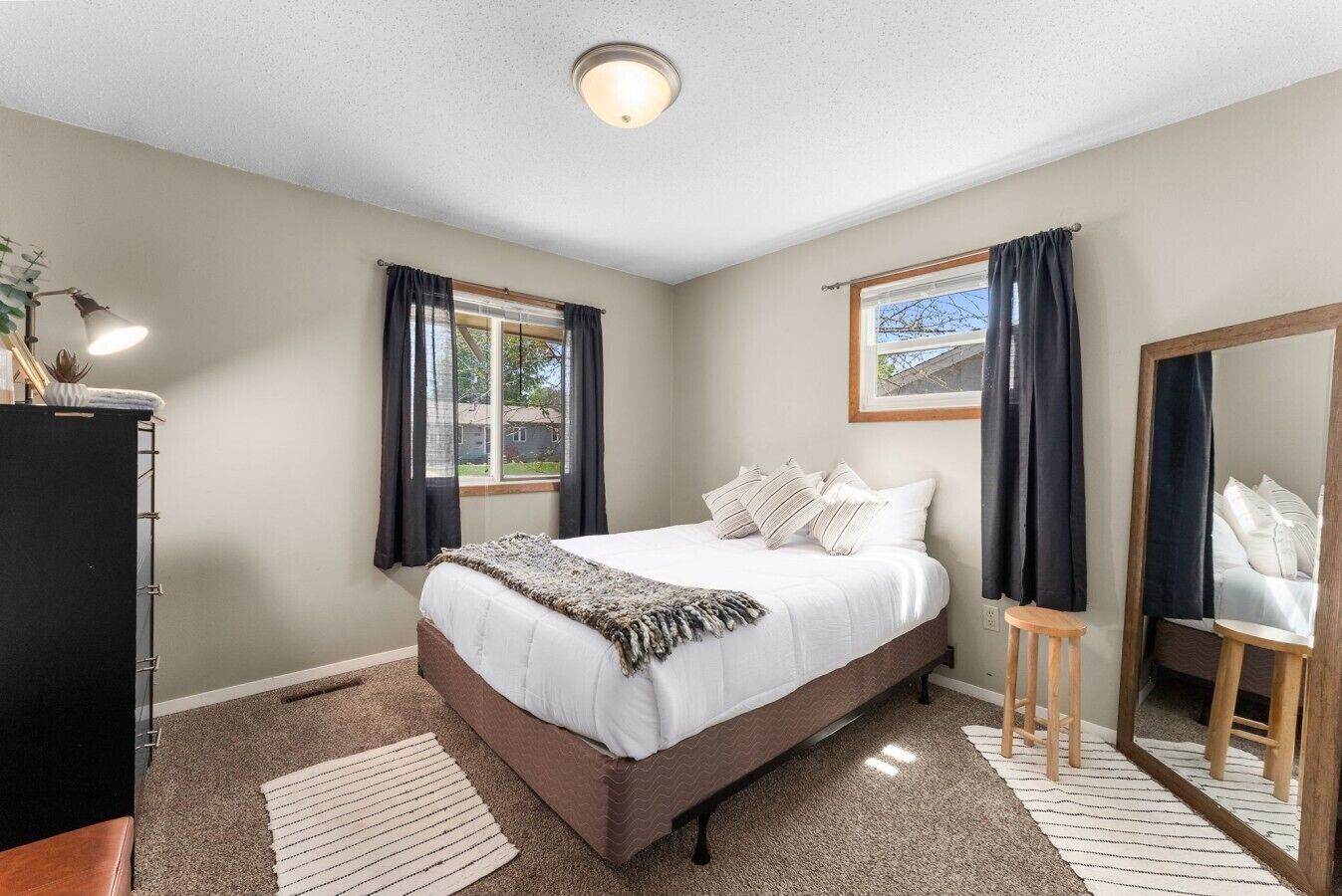 A bedroom with a bed, a mirror, a window with curtains, and a carpeted floor.