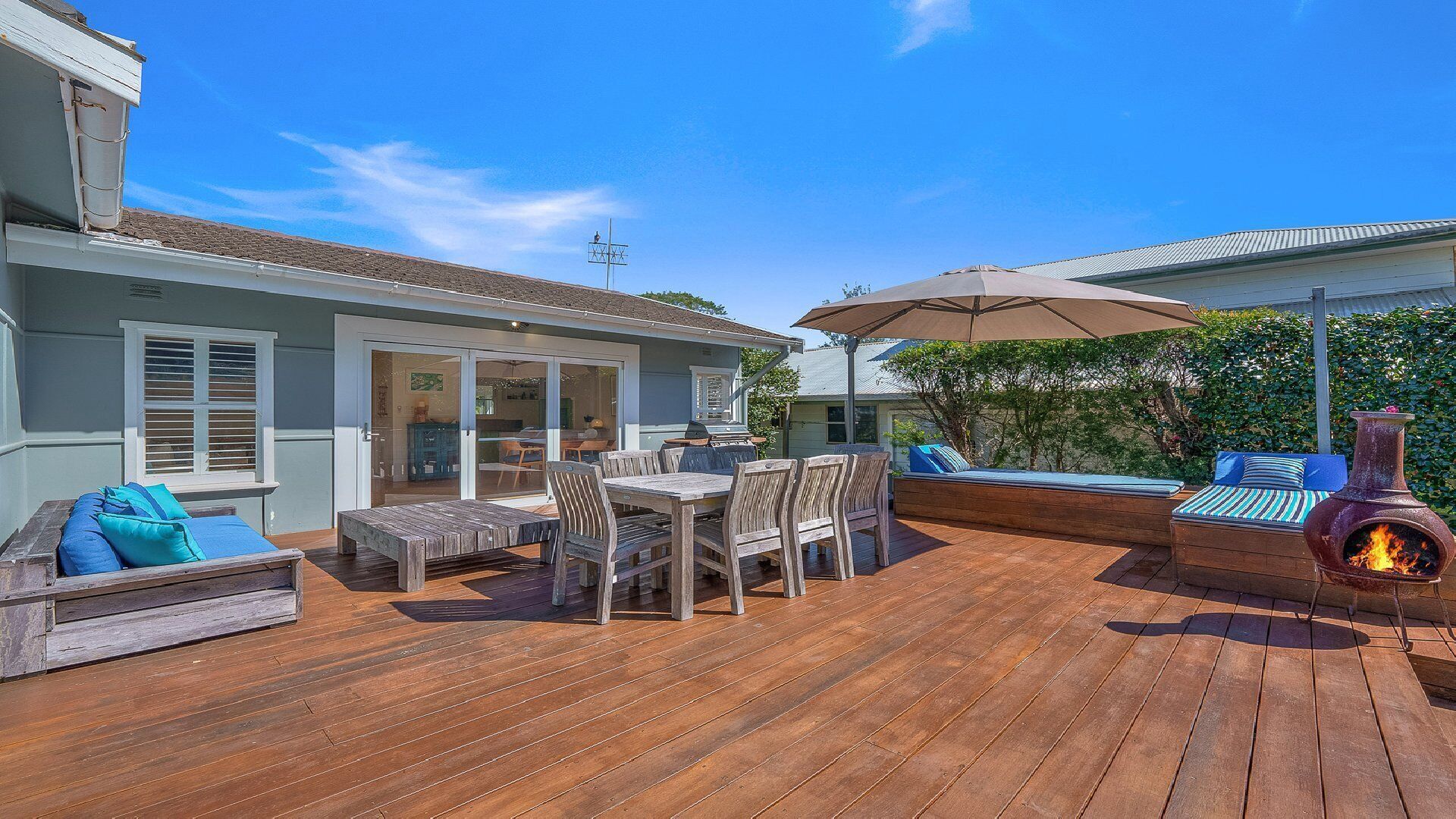 Eine Terrasse im Freien mit Holzdeck, einem Tisch mit Stühlen, einem Grill und einem Holzofen.