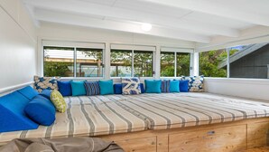 A sunlit room with a large window, a built-in bench with cushions, and a view of greenery outside. - MacMasters Malibu - Lakefront by HolidayCo. (MACMASTERS BEACH)