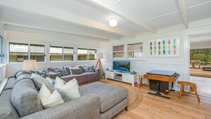 A spacious living room with a large sofa, a television, and a dining area with a table and chairs. - MacMasters Malibu - Lakefront by HolidayCo. (MACMASTERS BEACH)