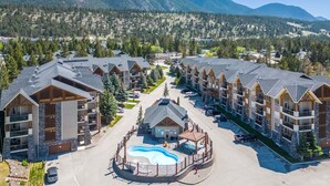 A resort with multiple buildings, a central pool area, and a mountainous backdrop. - Red Maple Retreat | Hot Tub | Pool | Gas Fireplace (Radium Hot Springs)