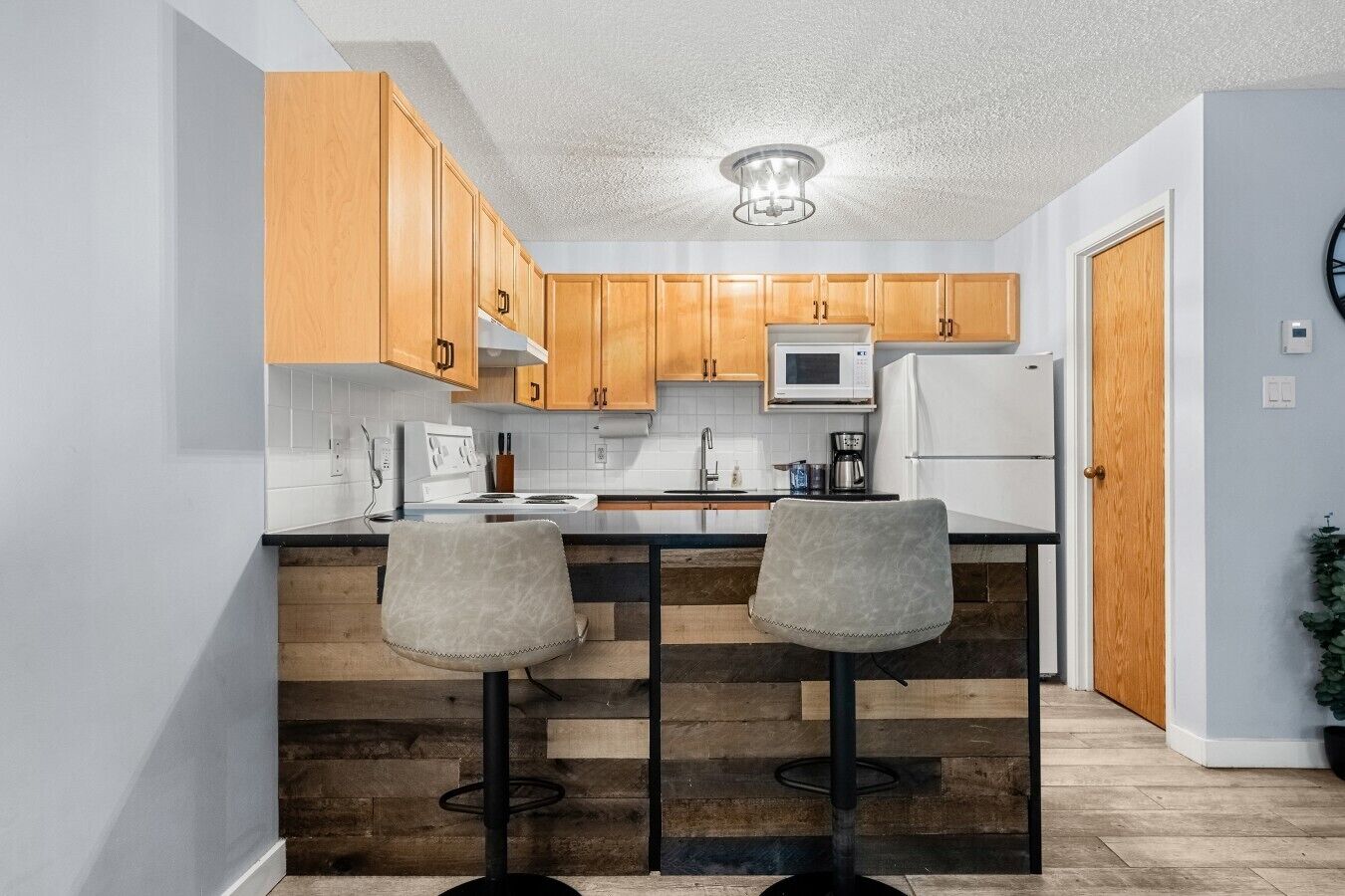 A kitchen with wooden cabinets, a microwave, a refrigerator, and two bar stools.