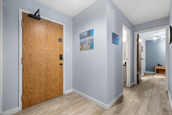 A hallway with a wooden door, light blue walls, and a wooden floor.