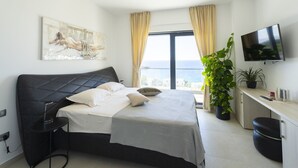 Ett modernt sovrum med en stor säng, ett skrivbord, en tv och utsikt över havet.