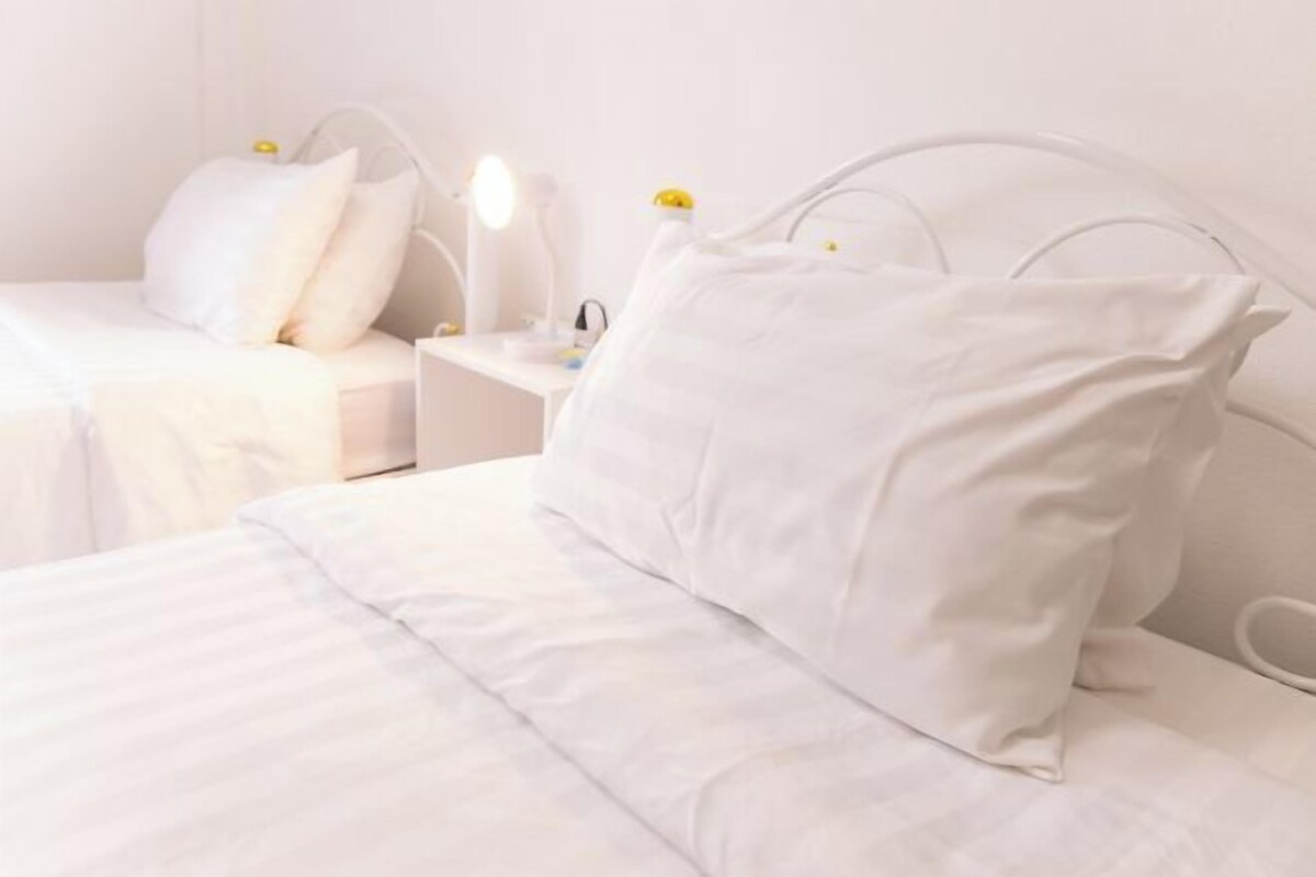 A white bed with a headboard, a bedside table with a lamp, and two pillows.