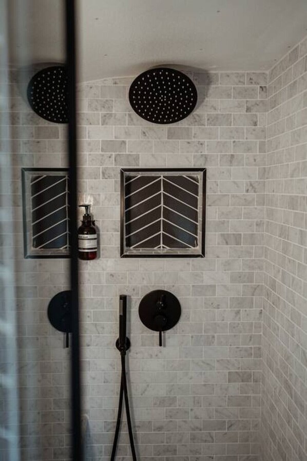A shower with two roundheads and two squareheads, a bottle of shampoo, and a handheld showerhead.