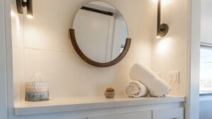 A bathroom with a white vanity, a round mirror, and two wall-mounted lights.