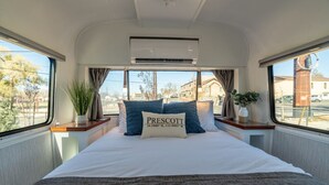 A bedroom with a bed, air conditioning unit, windows, curtains, and a plant.