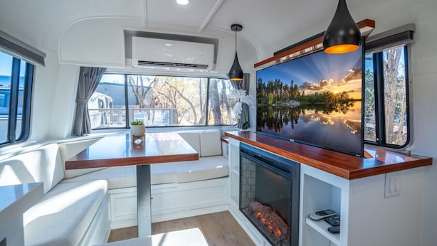 A modern RV interior with a dining area, a fireplace, and a large window with a scenic view.